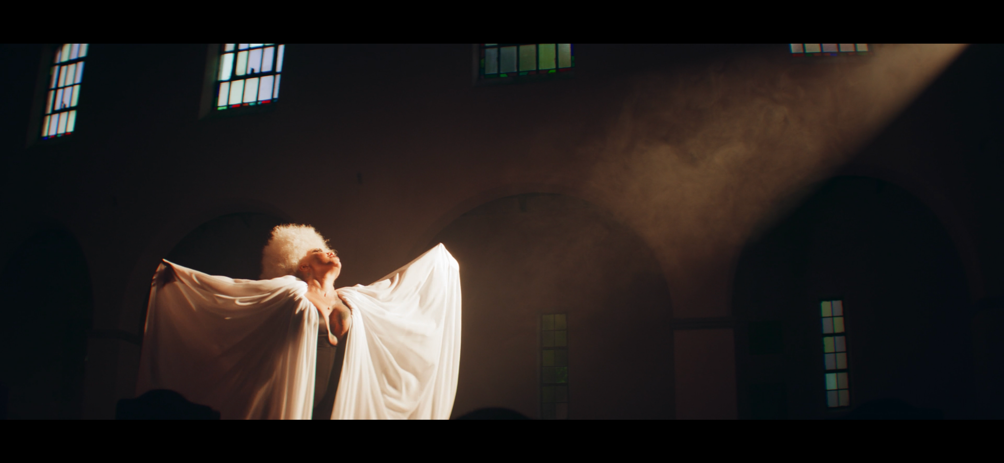 A performer in a flowing white outfit beneath a shaft of warm light